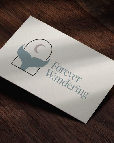 Visitenkarte mit aufgedrucktem Logo, das aus einem Torbogen in dem eine Walflosse mit Mond abgebildet ist. Daneben steht Forever Wandering geschrieben.